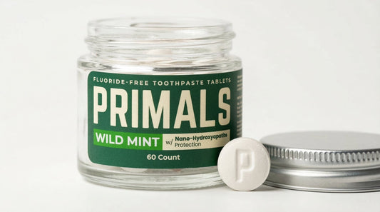 PRIMALS Wild Mint fluoride-free toothpaste tablets in glass jar with single nano-hydroxyapatite tablet and lid on white background